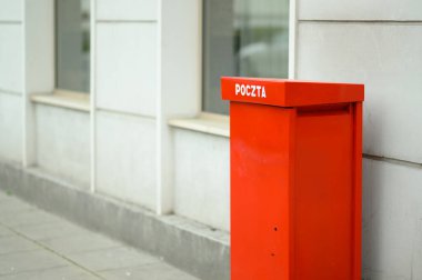 Açık bir günde 'poczta' etiketli canlı kırmızı bir posta kutusu çağdaş bir binanın yanında, dikkat çekiyor.