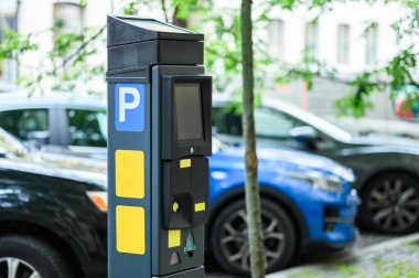 Park yerindeki araçlar ve yeşilliklerle çevrili bir parkmetre kaldırıma yerleştirildi..