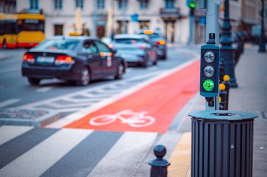 Yoğun bir şehir caddesinde akşam trafiğinin yoğun olduğu saatlerde arabalar beklerken, özel bir bisiklet yolunda bir bisiklet sinyali yeşile döner.