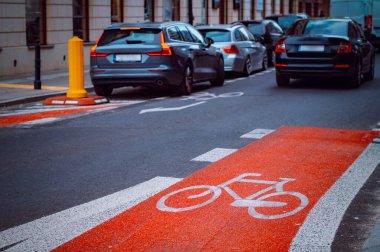 Parlak kırmızı bisiklet yolu gün içinde kalabalık bir şehir caddesinde park halindeki arabaların yanında belirgin bir şekilde işaretlenmiştir..