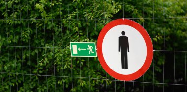 Bir inşaat alanında yemyeşil yeşilliklerin ortasında acil çıkış tabelasının yanında yaya girişi yasaktır..