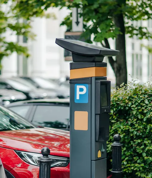 Parlak bir günde yemyeşil bir çevrede kırmızı bir aracın yanında bir parkmetre durur..