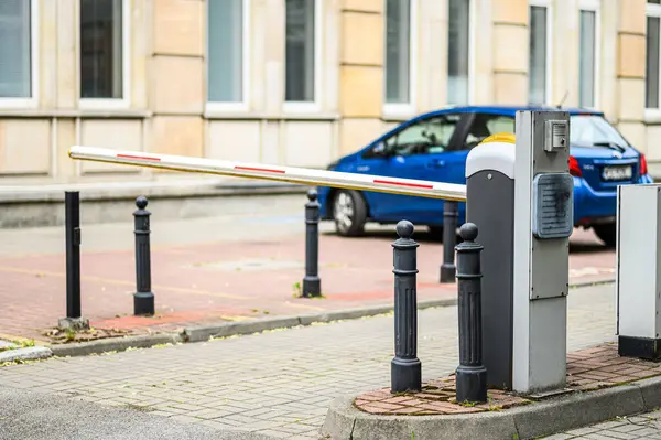 Bir araç, modern mimari unsurların yer aldığı bir bölgedeki park erişimini kontrol etmek için tasarlanmış bir güvenlik bariyerine yaklaşıyor..