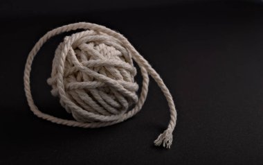 Sıkıca sarılmış beyaz bir ip topu siyah bir zemine dayanır. Karmaşık dokusunu ve ayrıntılarını minimalist bir ortamda gösterir..