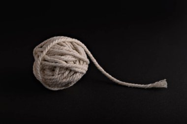 Bir ip topu karanlık bir yüzeyde oturur, dışa doğru kıvrılan gevşek bir uç, ilginç bir görsel kontrastlık ve doku yaratır..