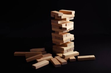 Bloklar uzun bir kuleye istiflenir, dikkatle dengelenir, oyun gecesi boyunca karanlık bir yüzeyde dağınık parçalarla çevrilidir..