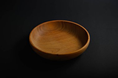 Tahta bir kase, düz kıvrımlarını ve doğal bitişini gösteren karanlık bir yüzeye dayanır. Sanatsal kaliteyi ve basitliği vurgular..