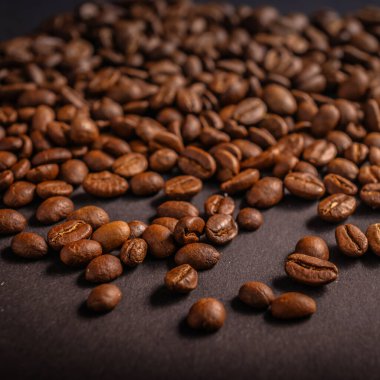 Koyu kavrulmuş kahve çekirdekleri dokulu bir yüzeye serpiştirilmiş, zengin renklerini ve şekillerini sıcak ışıkta vurguluyorlar..