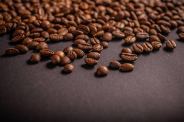 Kahverengi kahve çekirdekleri koyu bir arkaplana yayılır ve demlenme işleminden önce dokularını ve aromalarını sergiler..