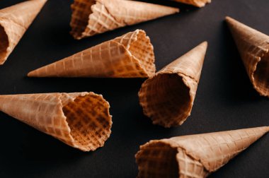 Çeşitli oryantasyonlarda waffle külahları siyah bir yüzeye uzanmış dondurma tatlarının eklenmesini beklerler..