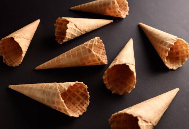 Waffle külahları koyu bir zemine saçılmış vaziyette dondurmacıları en sevdikleri tat ve malzemelerle doldurmaya davet ediyorlar..