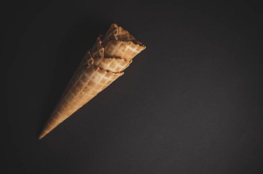 Koyu bir yüzeyde gevrek bir waffle külahı, keyifli bir ikram için lezzetli dondurmayla doldurulmayı bekliyor..