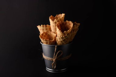 Birçok waffle külahı, çeşitli dondurma aromalarıyla doldurulmak üzere, koyu bir arka planda sunulan kırsal bir kovada istiflenir..
