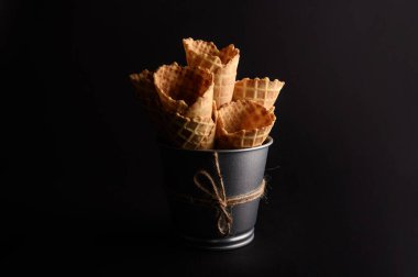 Waffle konileri metal bir kovada sanatsal olarak istiflenir ve karanlık bir arka planda büyüleyici bir görüntü oluştururlar..