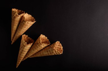 Koyu bir zemin üzerinde sergilenen dört waffle konisi, leziz dondurmaları tutmak için mükemmel olan desen ve tasarımlarını ön plana çıkarıyor..