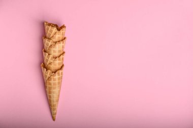 Dört waffle külahı düzgün istiflenmiş, parlak pembe bir zemin üzerinde taze dokularını sergiliyorlar, dondurma tutmak için mükemmel..