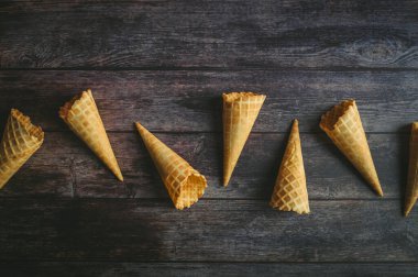 Waffle külahları kırsal ahşap bir yüzeye düzgün bir şekilde dizilmiş, gevrek dokularını ve dondurmaları tutmak için mükemmel şekillerini sergiliyorlar..