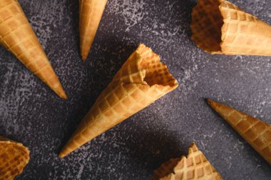 Waffle külahları karanlık bir yüzeyde gelişigüzel dizilir, bazı ısırıklar gösterir, lezzetli dondurmalar için hazırlanmayı önerir..