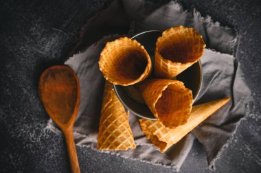 Waffle külahları, ahşap bir kaşıkla bir kasenin içinde, koyu renkli bir yüzeye yerleştirilerek, davetkar bir düzen oluşturulur..