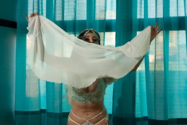 Woman dances with bodily expression holding a translucent veil in her arms while a bit of her face peeks through the vaporous fabric