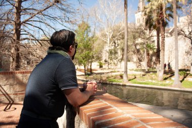 Beyaz Latin bir adam San Antonio 'nun sokaklarında mola veriyor. Nehir kenarındaki yürüyüşte. Önlem olarak maske takıyor.
