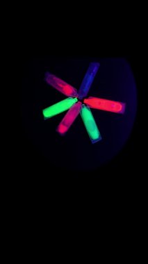 Neon pigment tüplerinin soyut çiçekleri dönen ışıklar siyah ışık kilidi şafak kamerası tarafından aydınlatılır.