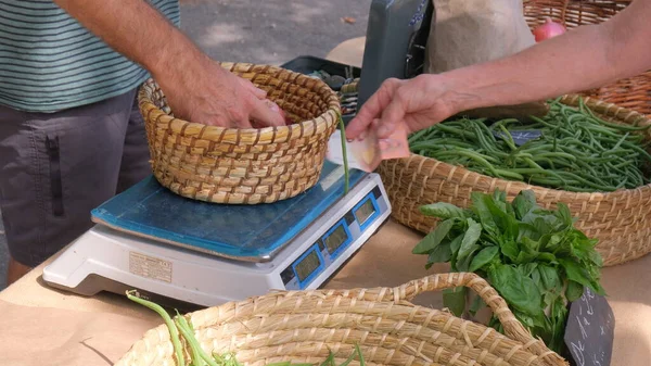 Close up of farmers market with baskets of green beans, hands weighing purchase and paying with euro. High quality photo