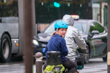 15 Mayıs 2023 Paris Fransa. Genç kız yağmur ve trafikte ebeveyn bisikleti süren bir yolcu. Bisikletler Paris 'te alternatif bir ulaşımdır..