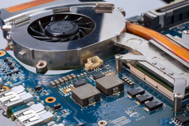 Laptop soğutma teknolojisi. Bir bilgisayar anakartının detaylı bir görüntüsü, işlemci için soğutma vantilatörü, yonga setleri ve devre kartı karmaşık mühendislik ve bileşik materyalleri sergiliyor.