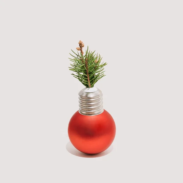 Ornament red Xmas bauble with light bulb cap and a small Christmas tree branch isolated on a white background. New Year greeting card in a minimalist style.