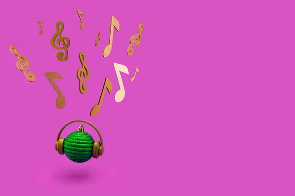 Green Christmas bauble with headphones, musical notes and violin key on a vibrant purple background. Concept of Christmas, New Year and winter holidays party, music and happiness.