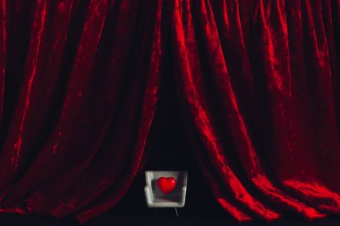 Real velvet cloth stage silk curtain and a little red heart in a gray armchair. Throne of Hearts. The concept of theater, love and romance.