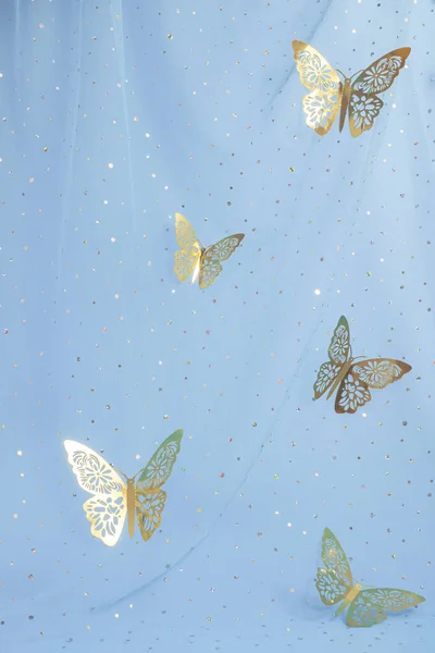 Aesthetic blue background with tulle, sequins and golden butterflies.