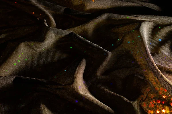 Magic, fairy tale dark background of black tulle fabric and holographic foil with colorful stars. Fashion, love and mystery concept.