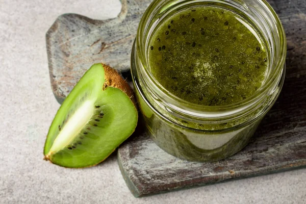 Homemade kiwi jam in a jar and kiwi slyces on concrete background with copy space.
