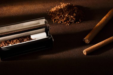 Hand-rolled cigarette, rolling machine, cigarillos, scattered tobacco on background, cigarette roll with filter, cigarette filters