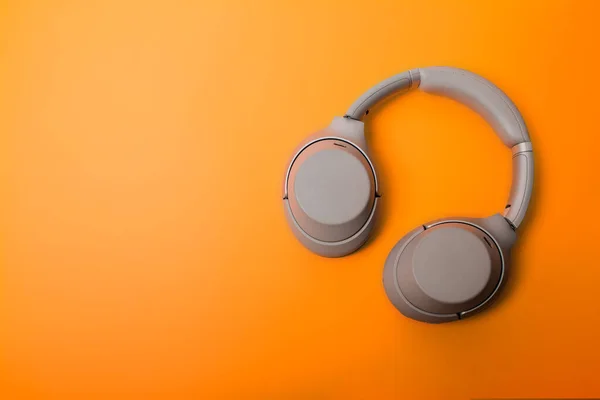 Light gray wireless over-ear headphones on an orange background. Headphones for playing games or listening to music. Noise canceling headphones. Top view. Copy space