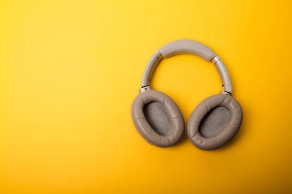 Light gray wireless over-ear headphones on an yellow background. Headphones for playing games or listening to music. Noise canceling headphones. Top view. Copy space