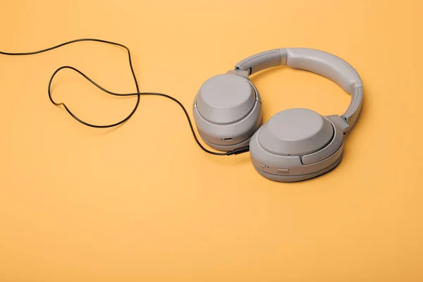 Light gray wireless on-ear headphones with the ability to connect via wire on a peach background. Headphones for playing games or listening to music. Noise canceling headphones. Top view. Copy space