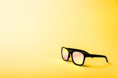 Black sunglasses with Multicolor Mirror Lens on sunny yellow background. Polarized sunglasses with UV protection. Copy space.