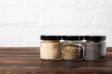 Bright fragrant spices in glass jars of different sizes on a wooden table. Proper storage of spices.