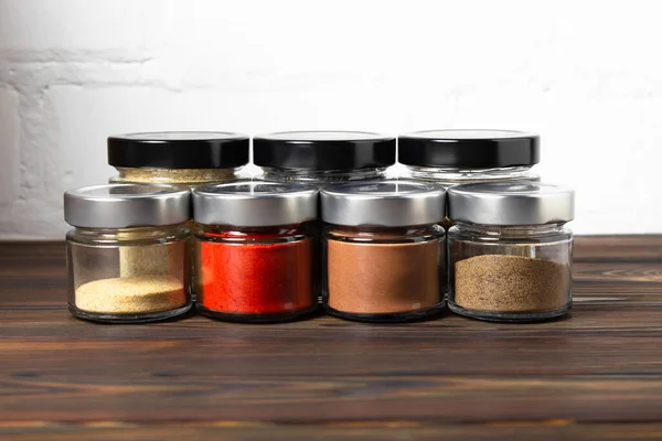 Bright fragrant spices in glass jars of different sizes on a wooden table. Proper storage of spices.