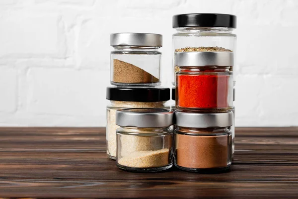 Bright fragrant spices in glass jars of different sizes on a wooden table. Proper storage of spices.