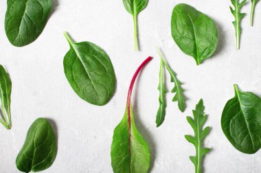 Pattern of salad mix leaves, arugula, spinach, chard on a gray background.