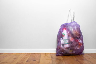 Gri bir duvarın yanındaki ahşap zeminde mor çöp torbası. Ev temizliği. Çöp ayıklama teması. Çevreye önem vermek