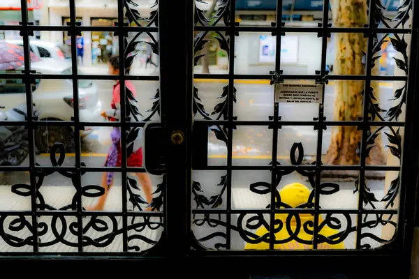 Kırmızı elbiseli bir kadın bir apartmanın güvenlik kapısının önünden geçiyor.