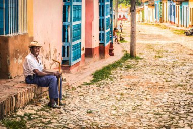 Trinidad, Küba - 15 Temmuz 2018: 18. yüzyılda hala taş kaldırımlı caddeleri olan eski bir İspanyol sömürge kasabası. Yaşlı bir adam kaldırımda oturuyor.