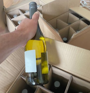 Birisi internetten sipariş edilen bir şişe şarabı bir teslimat kutusundan çıkarıyor.