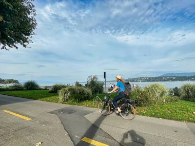 Geneva, Switzerland - September 14 2021: a person with helmet on on a bike is cycling along the lake on a bike trail clipart