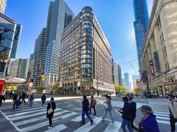 Торонто, Канада - 24 октября 2022 года: люди, идущие по пешеходному переходу улицы в центре города с магазинами и магазинами вокруг